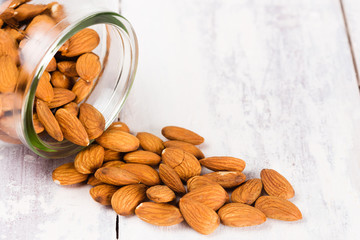 Almonds in a jar, spilled on a white vintage table. the jar is lying down on a white table.