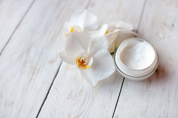 Fototapeta na wymiar pot of face cream and beautiful white orchid flowers on white wooden table