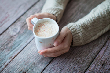 woman's hands holding a cup of coffee on the wooden table