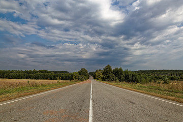 Asphalted road against the blue sky with clouds.