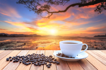 White coffee cup and coffee beans on wood table and view of suns