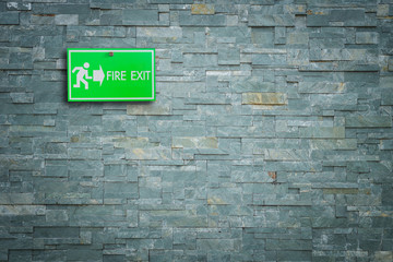 Fototapeta na wymiar Green fire exit sign on stone wall