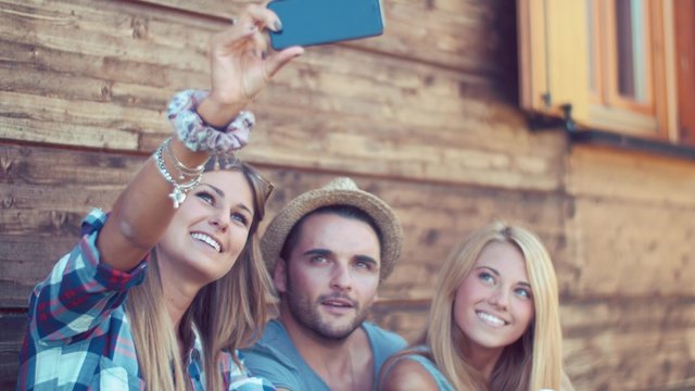 Handheld shot of friends taking selfie in front of wooden wall
