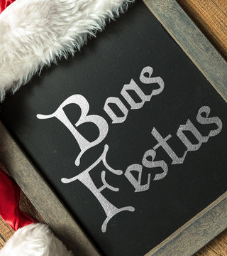 Happy Holidays (in Portuguese) written on blackboard with santa hat