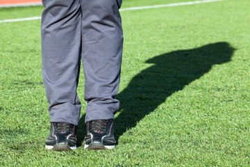 Fototapeta premium Low angle front view of female legs wearing running shoes while standing on green grass field, copyspace