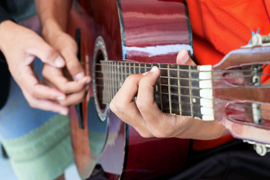 blurred man's hands playing acoustic guitar, and teaching guitar