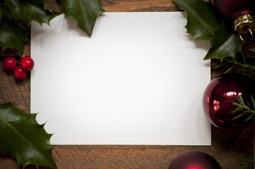 Photo of empty christmas card and holly leafs on old wooden table. Warm natural light