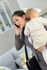 Busy businesswoman talking on phone and holding baby in arms © goodluz