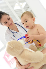 Baby in doctor's office playing with stethoscope and teddy bear