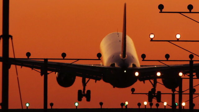 HD footage of a twin engine jet plane landing in silhouette against an orange sunset sky, followed by a defocus / camera blur out.  Jet engine audio included.