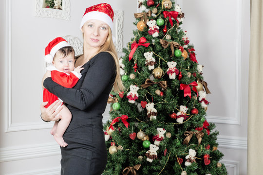 Portrait of a woman with a child near the Christmas tree. Mom holds daughter on hands.