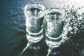 Vodka shot glass on wet black surface.