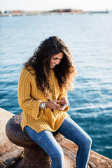 Young woman sitting on pier and chatting over phone