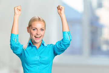 Pretty young blonde woman throwing her arms up into the air and laughing in jubilation at her success or victory