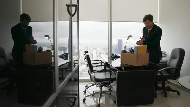Businessman recently hired for corporate job moves into his new office. He takes out files, folders and writing articles from a box and puts them in order on his desk. Wide shot