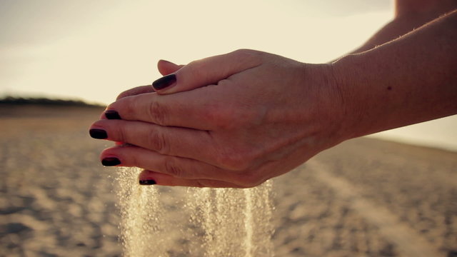 Female hand scatter the sand  at  sunset 