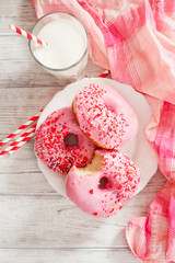 
sweet donuts with strawberry and cherry pink icing and milk on a wooden background