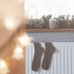 Winter woolen socks drying on a heater, christmas lights, decorations and hot drink 