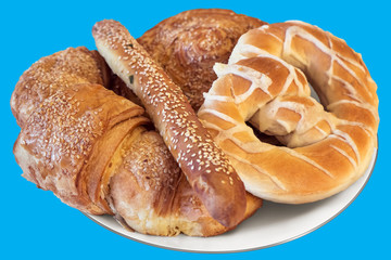 Plate of Pretzel and Croissant Puff Pastry Sprinkled with Sesame Seeds, Isolated on Blue Background.