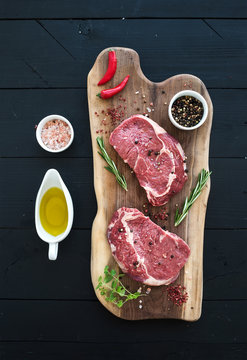 Raw fresh meat Ribeye steak entrecote and seasonings on cutting board over dark wooden background
