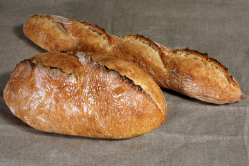 two white loafs of different shapes lie on the grey linen tablec