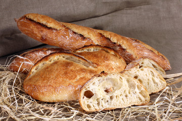 white loaves of different shapes lying in straw on grey linen ta