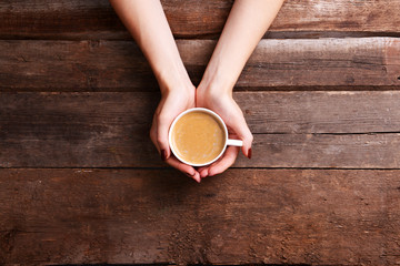 Female hands holding cup of coffee on wooden background