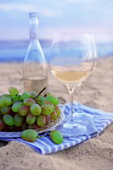 Romantic composition of white wine and grape on sandy beach