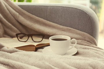 Cup of coffee with book on sofa in room