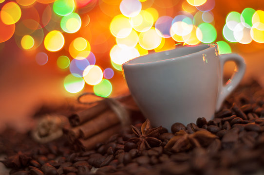 Christmas coffee: cup among coffee beans in front of christmas light