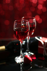 Setting of glasses with wine, bottle and a gift in the box, on red blurred background