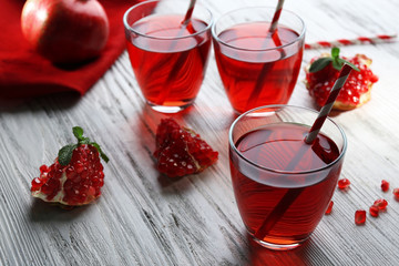 Three glasses of tasty juice and garnet fruit, on wooden background