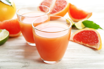 Two glasses of citrus juice and fresh fruits on light wooden background