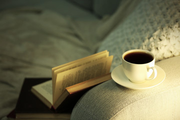 Cup of coffee with books on comfortable sofa, close up