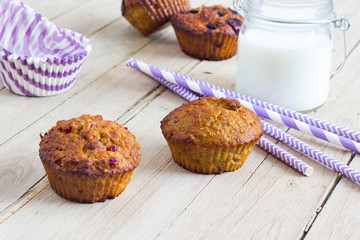 Freshly baked healthy otmeal muffins with berries. Purple baking decorations and milk in the background.