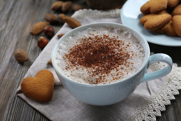 Cup of hot cacao on cotton serviette with cinnamon, almonds and heart shaped cookies, close up