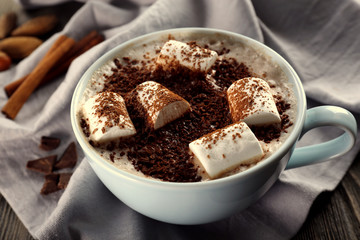 Cup of hot cacao with marshmallow, cinnamon and nuts on blue cotton serviette, close up