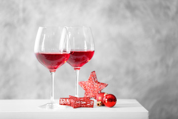 Two glasses of red wine with christmas accessories on grey wall background