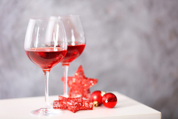 Two glasses of red wine with christmas accessories on grey wall background