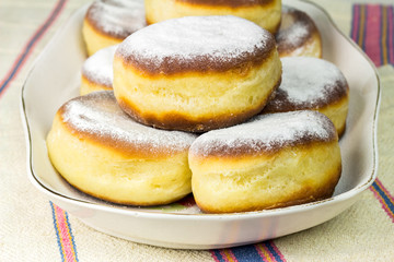 Group of fresh donuts sprinkled with powdered sugar in plate on old ukrainian linen tablecloth