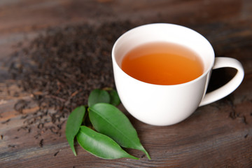 Ceramic cup of tea with scattered tea leaves around on wooden background