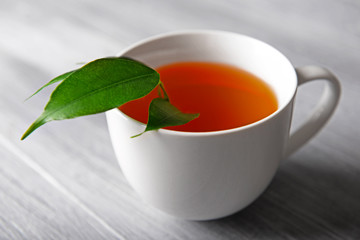 Ceramic cup of tea with green leaves on light wooden background