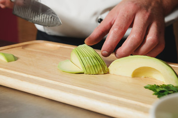 chef cutting avocado on table - obrazy, fototapety, plakaty