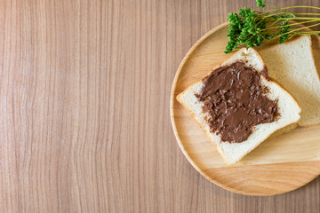 Chocolate spread on slice of bread on the wood plate. Top view with copy space.