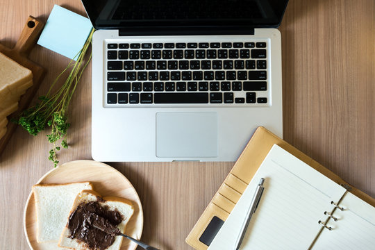 Working Table With Laptop, Notebook, Post It Note, Pen And Breakfast With Sliced Bread With Chocolate Spread. Top View.