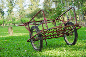 Fototapeta na wymiar old red steel cart on the green grass field