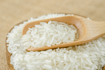 Raw rice in wooden bowl with wooden spoon.