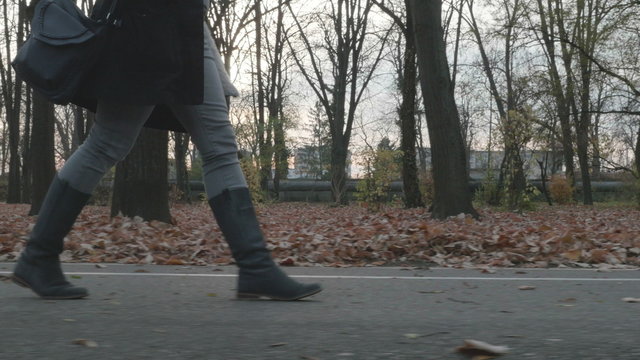 4k - Young beautiful woman in long boots taking a walk on an alley in the park