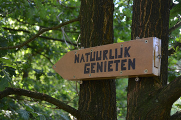 Wooden arrow sign with words Natuurlijk Genieten attached to tree