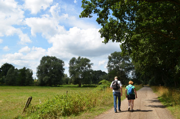 Man and woman hiking on a gravel road next to a meadow